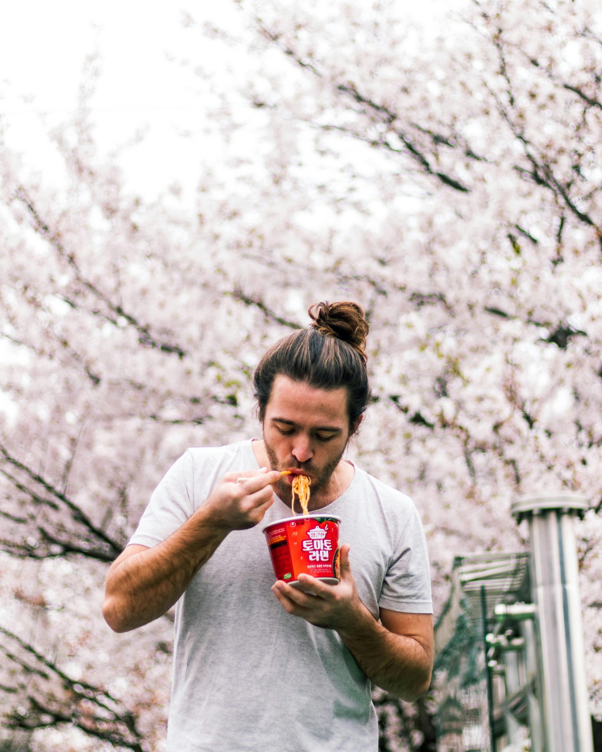 Man eating cup noodles amidst cherry blossoms in Seoul, capturing the essence of Korean street food culture.